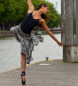 A ballet dancer pirouetting in a city location beside a river